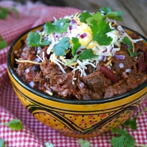 Chocolate Chipotle Colorado Style Chili in a ceramic golden bowl with cheese and cilantro on top.