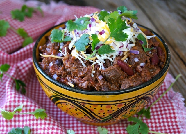 Chocolate Chipotle Chili in a ceramic golden bowl with cheese and cilantro on top.