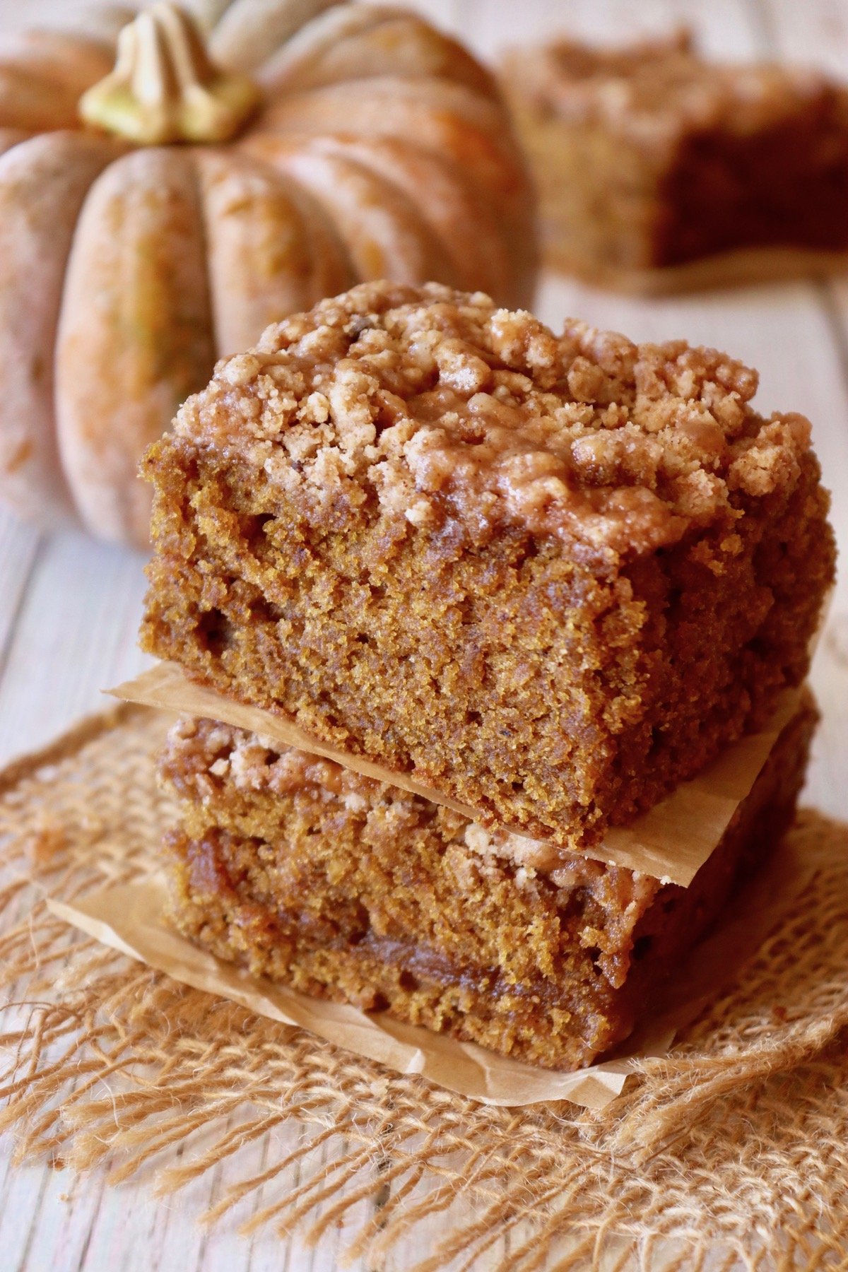 Two stacked pieces of pumpkin coffee cake with a dull orange pumpkin in the background.