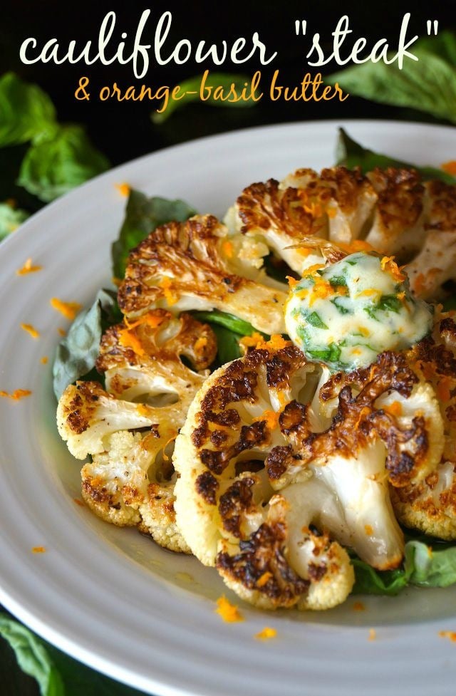 Cauliflower Steak with Orange-Basil Butter on a white plate surrounded by basil leaves.