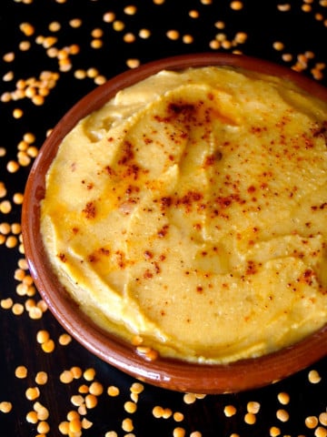 Terra cotta bowl filled with lentil hummus, sprinkled with paprika and drizzled with olive oil.