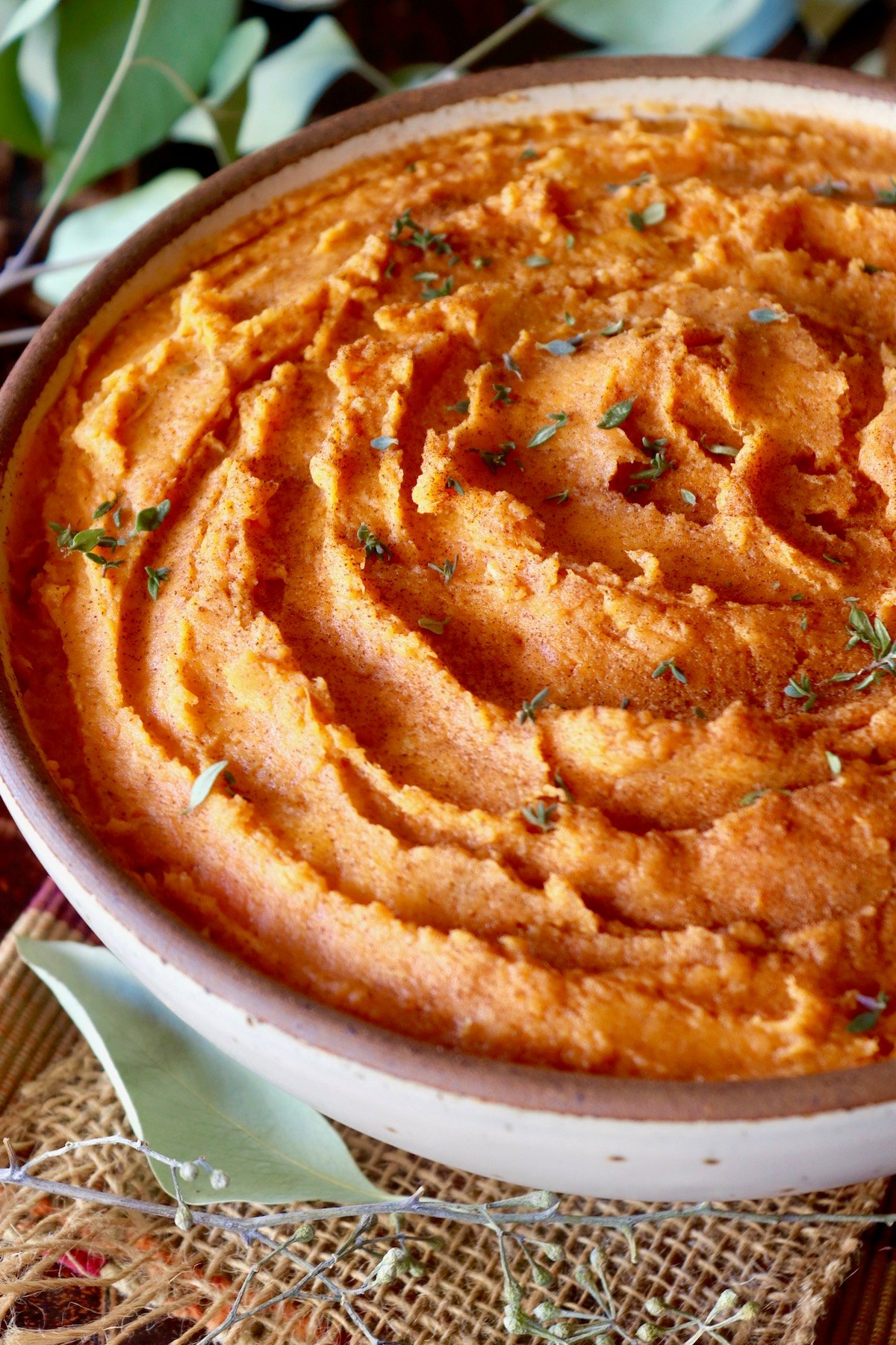 Close up of mashed sweet potatoes with fresh ginger in a beige ceramic serving bowl.