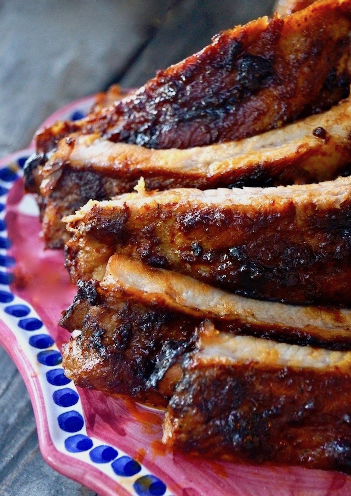 Smoky, Sweet and Spicy Pork Ribs piled on a dark magenta platter on a wood table.