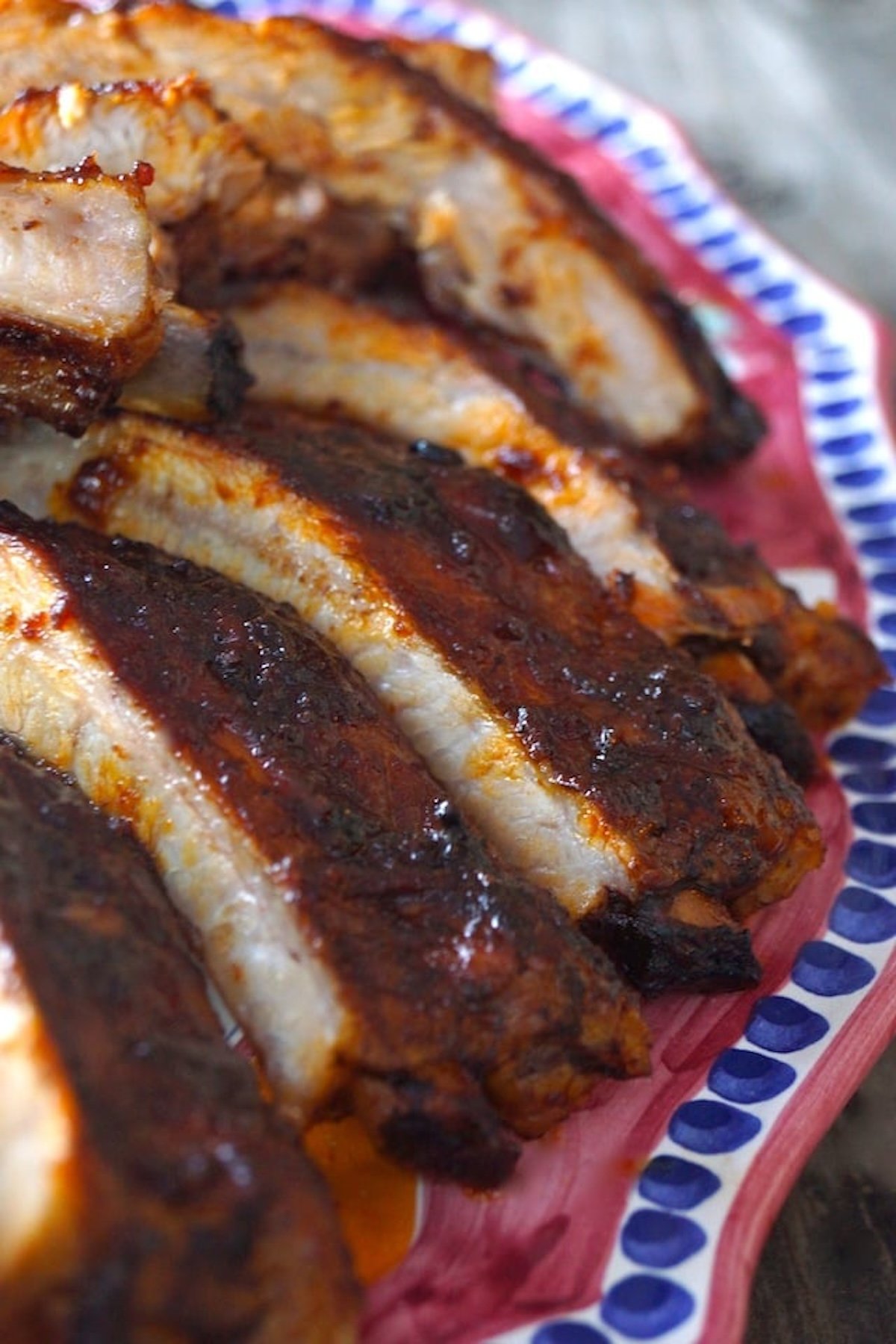 Several Pork Ribs on a dark pink platter with blue edges.