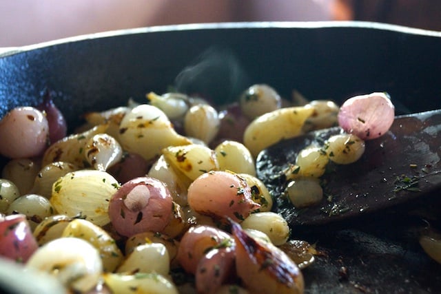 pearl onions in cast skillet with wooden spatula