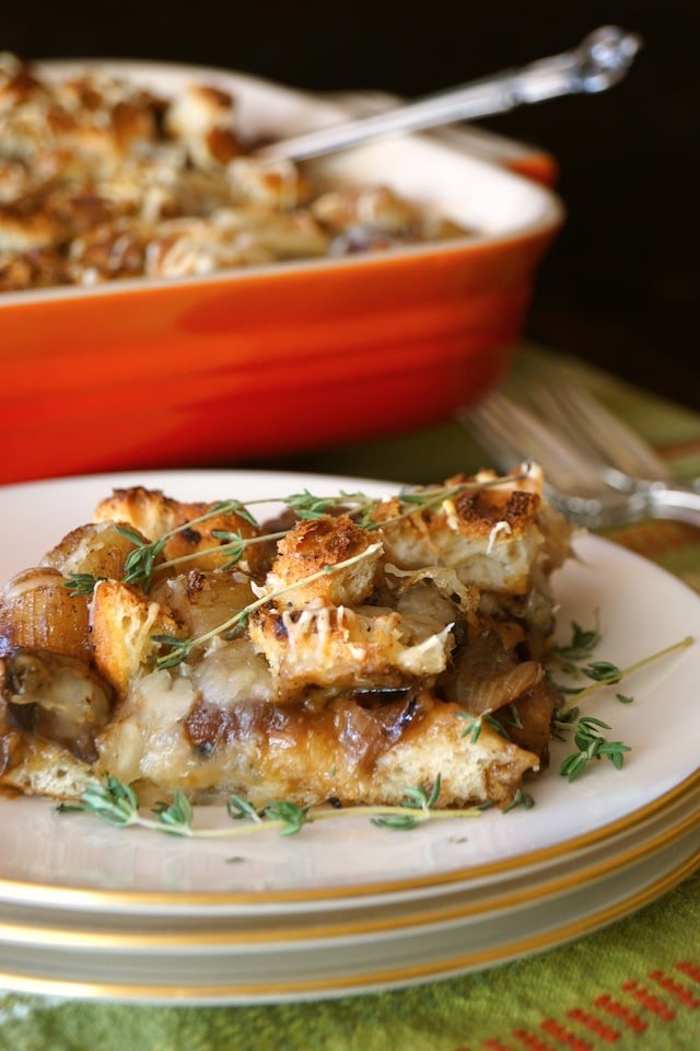 French Onion Mushroom Casserole Recipe sliced on a white plate with green thyme sprig and red dish in background