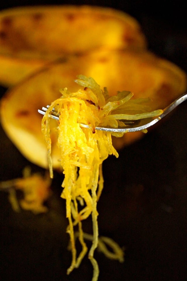 A fork full of cooked spaghetti squash in front of spaghetti squash halves.