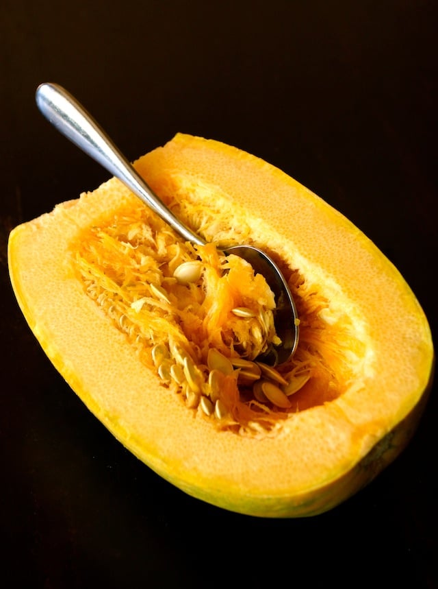 Half of a spaghetti squash with large metal spoon to remove seeds