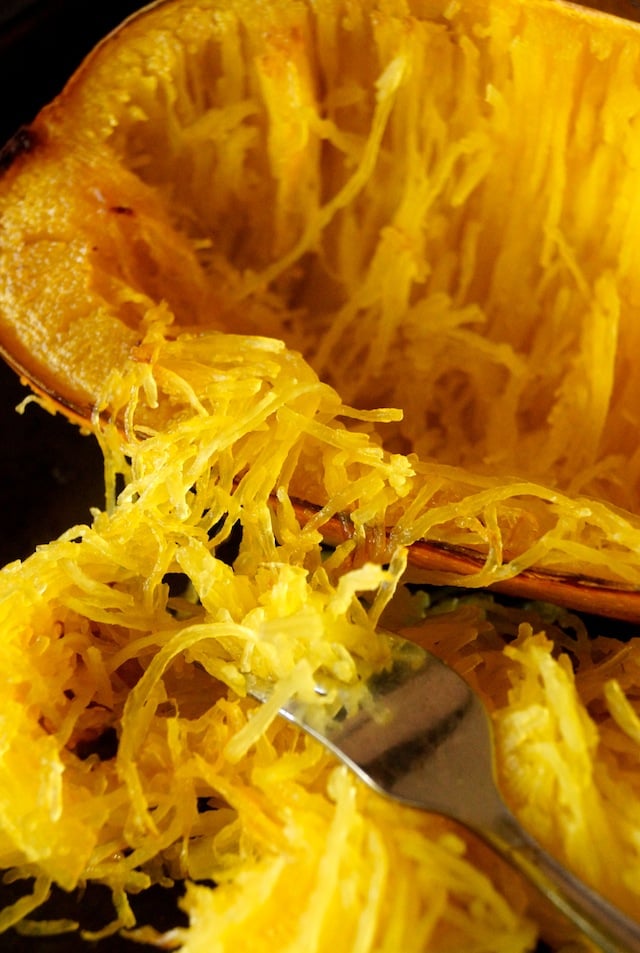 Cooked Spaghetti squash being removed from the inside of its skin with a fork.