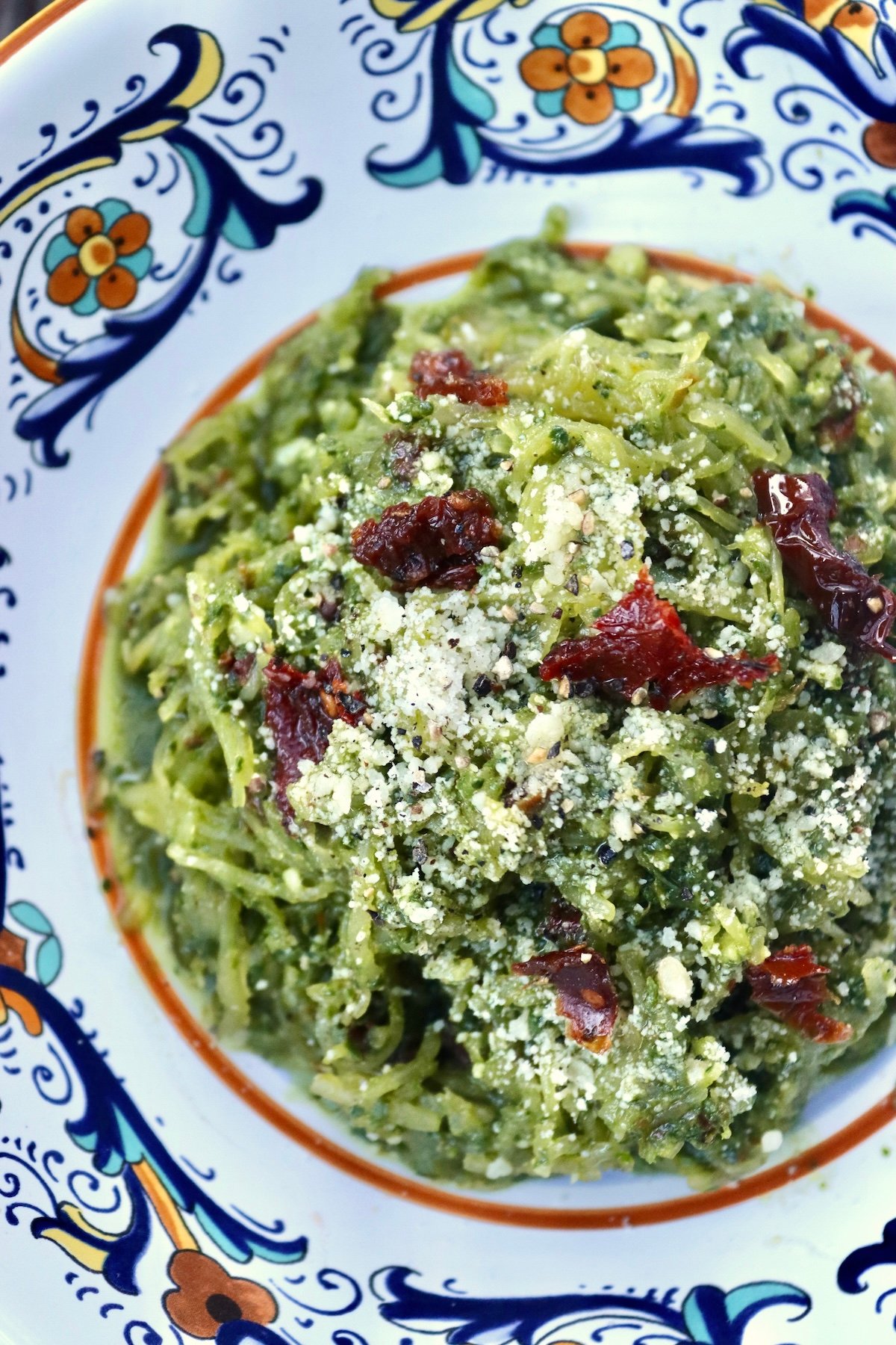 Italian painted ceramic bowl with spaghetti squash tossed with pesto made of spinach and bits of sun-dried tomatoes on top.