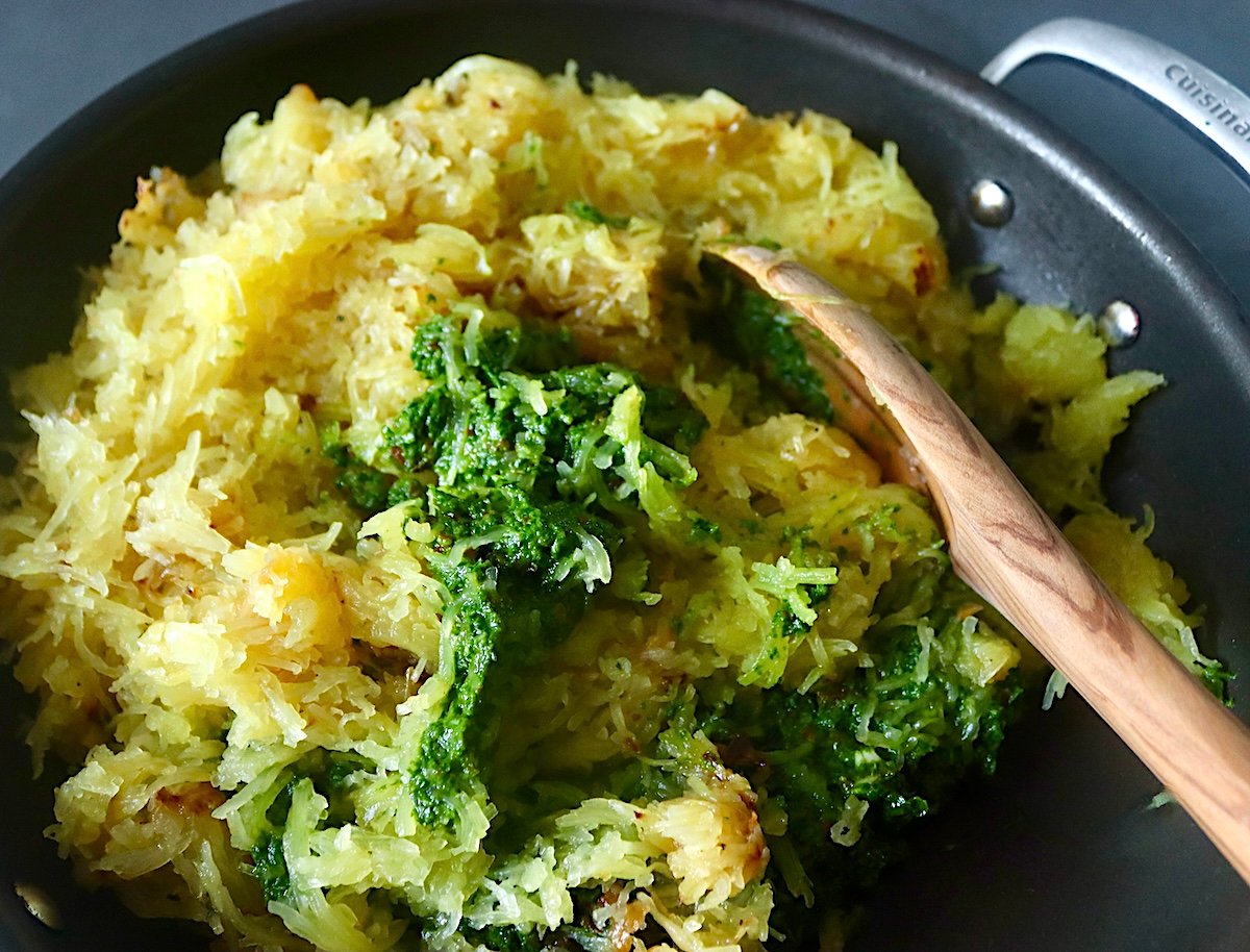 Spaghetti squash and spinach pesto in a saute pan with a wooden spoon.