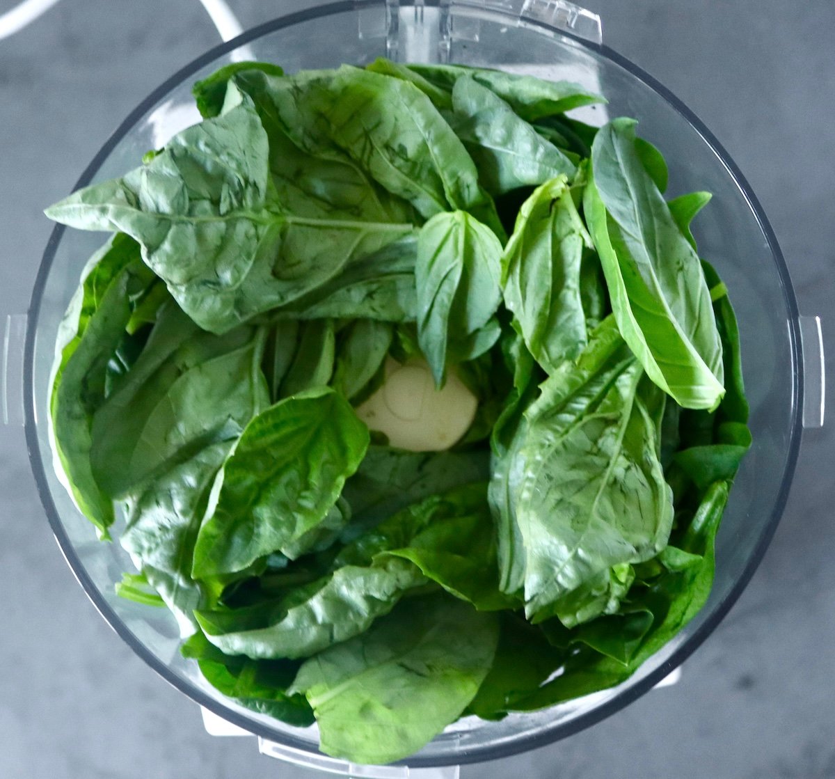 Spinach leaves and basil leaves in a food processor bowl.