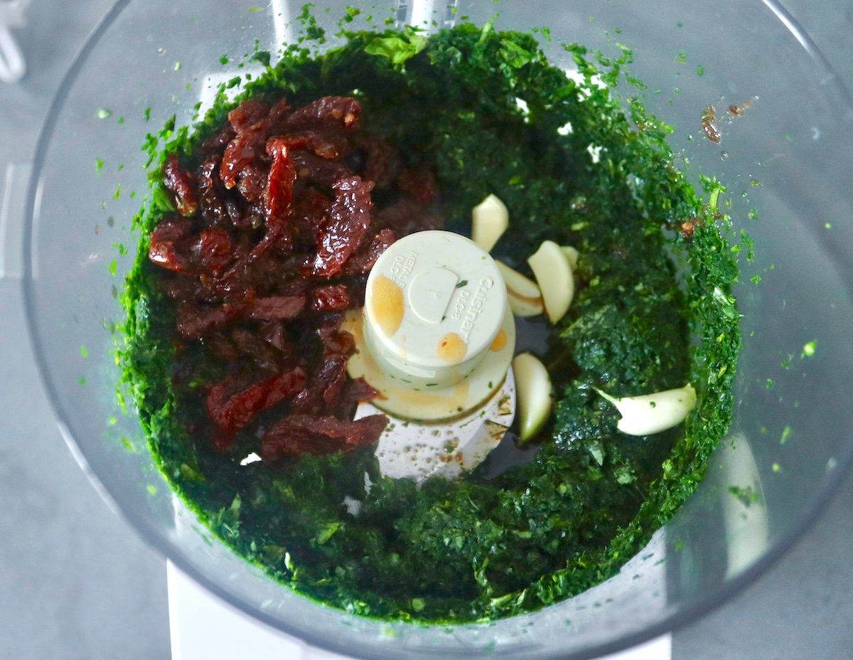 Finely chopped spinach and basil, sun-dried tomatoes and garlic, in a food processor bowl.