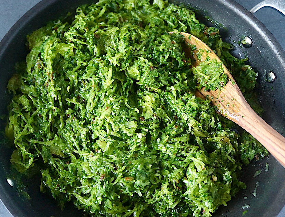 Spaghetti squash mixed with spinach pesto in a saute pan with a wooden spoon.