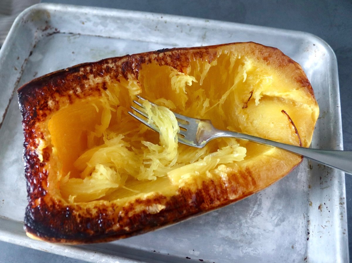 Half a roasted spaghetti squash with a fork in the center with some of the strands from the flesh.