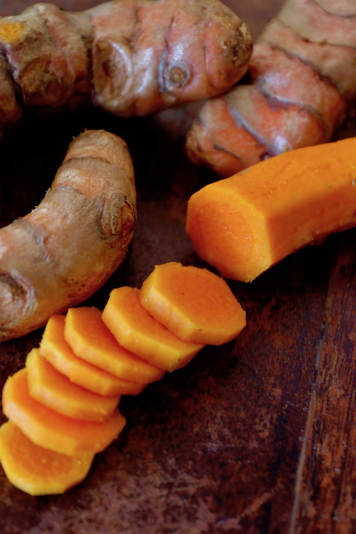 Sliced turmeric root that looks like a carrot, on dark wood board.