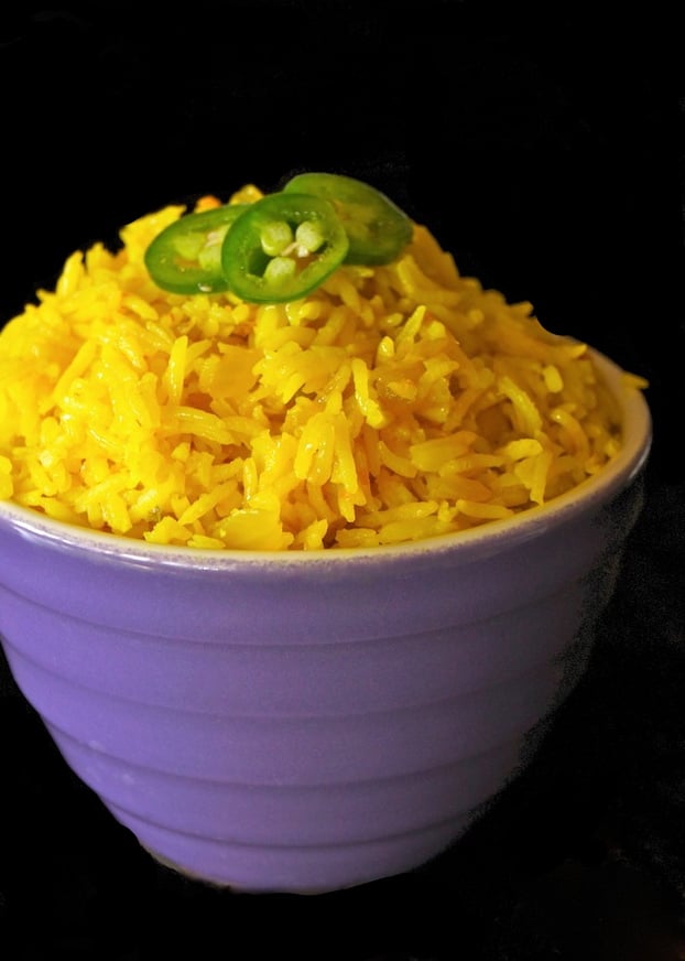 Purple bowl with yellow rice with rice with sliced alapenos on top.