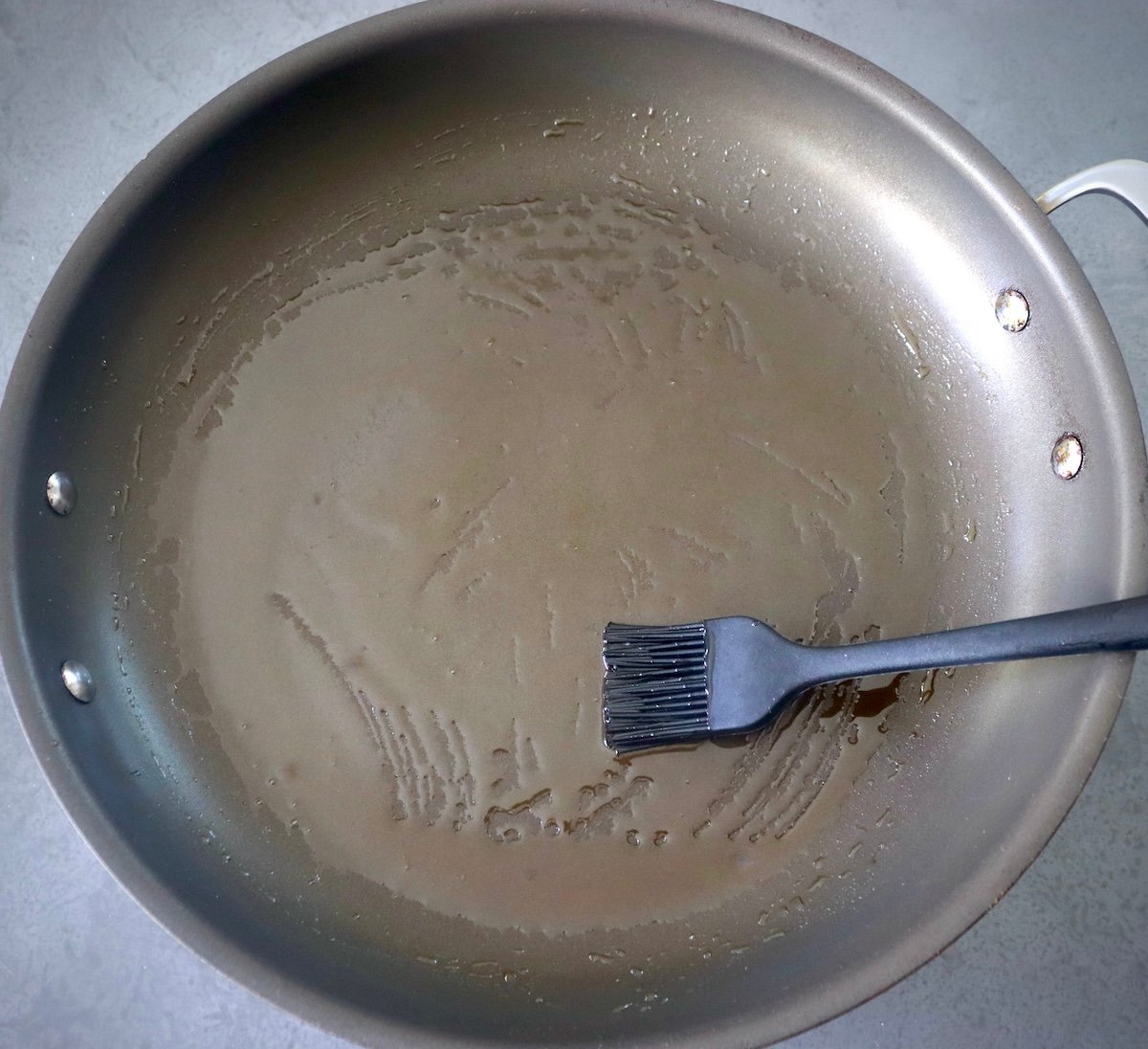 Large skillet with black silicone basting brush and oil.