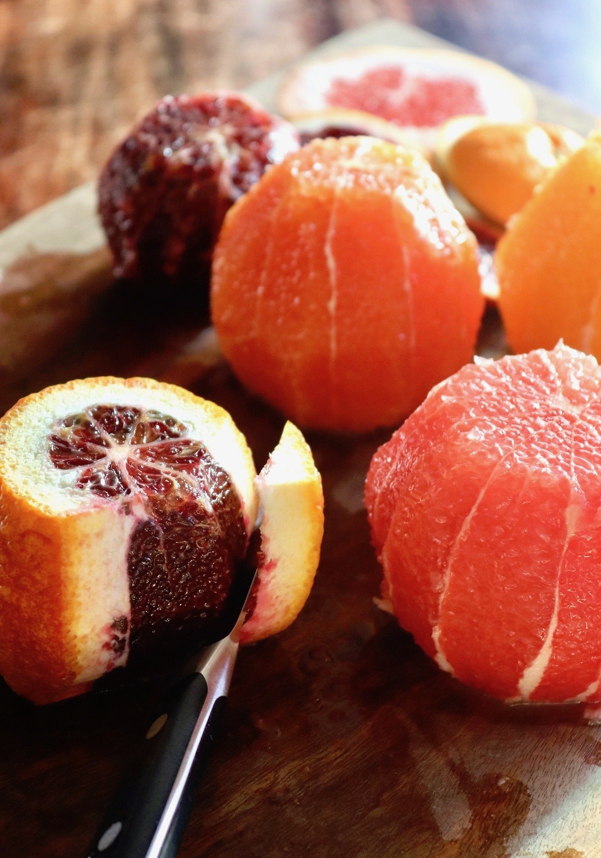 blood orange being peeled with a knife on cutting board