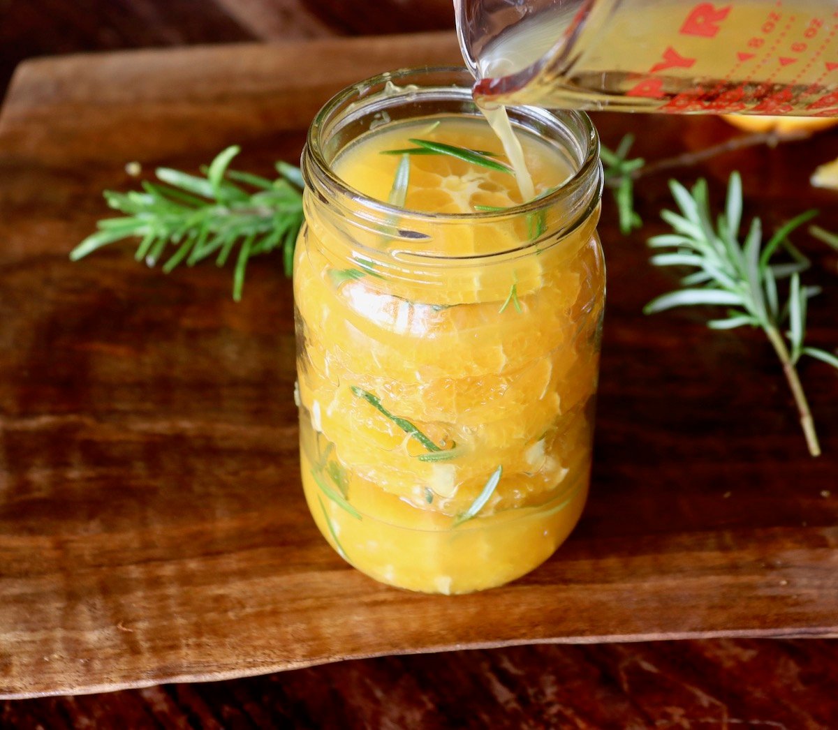 Jar with orange slices with orange juice being poured into it.