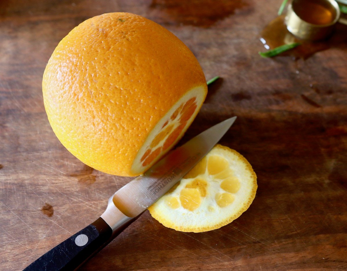 Top of an orange being sliced off, on cutting board.