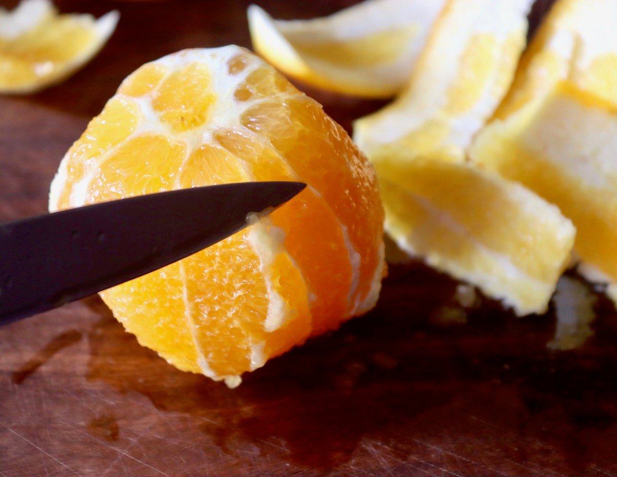 Orange with skin cut off and paring knife cutting off pith.