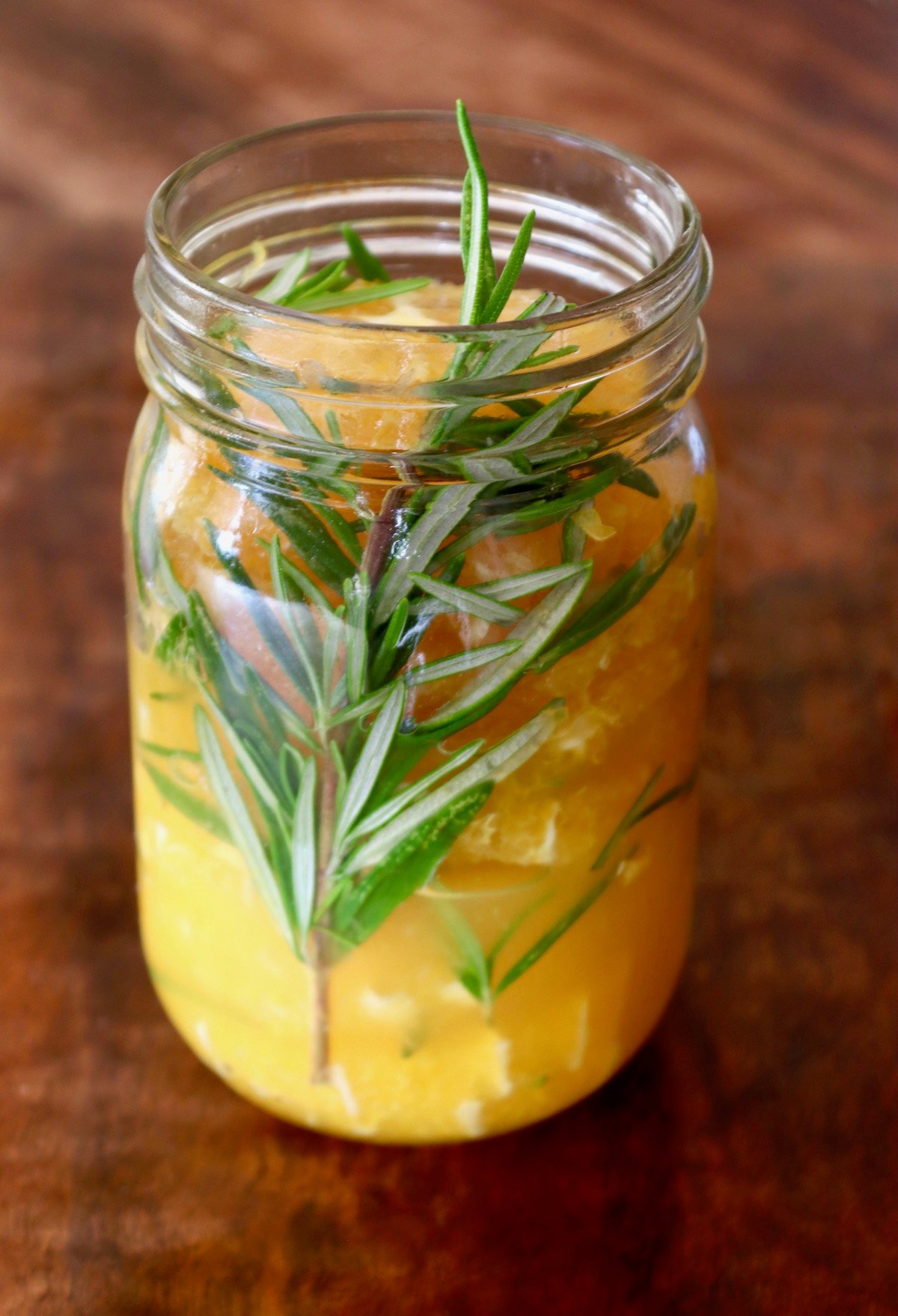 Jar filled with orange slices and rosemary sprig.