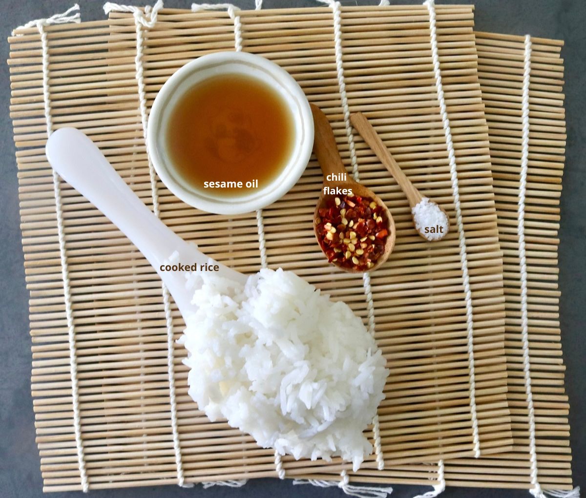 Ingredients for crispy rice on sushi mat including sesame oil. cooked rice, chili flakes and salt.