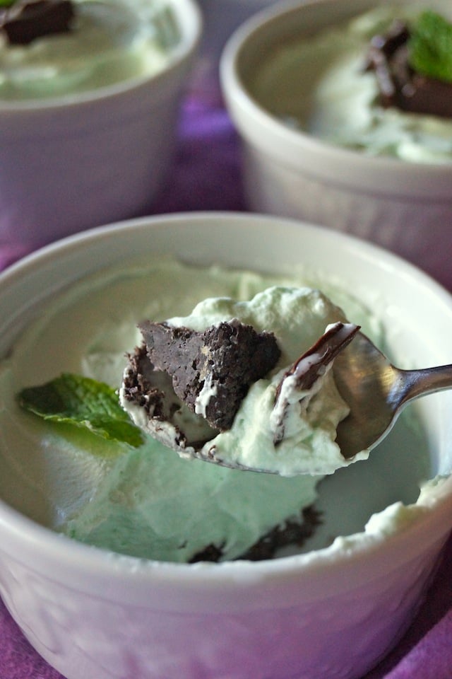 Individual Grasshopper Mousse Pies in white ramekins, with one bite with Oreo cookie crust in a spoon.