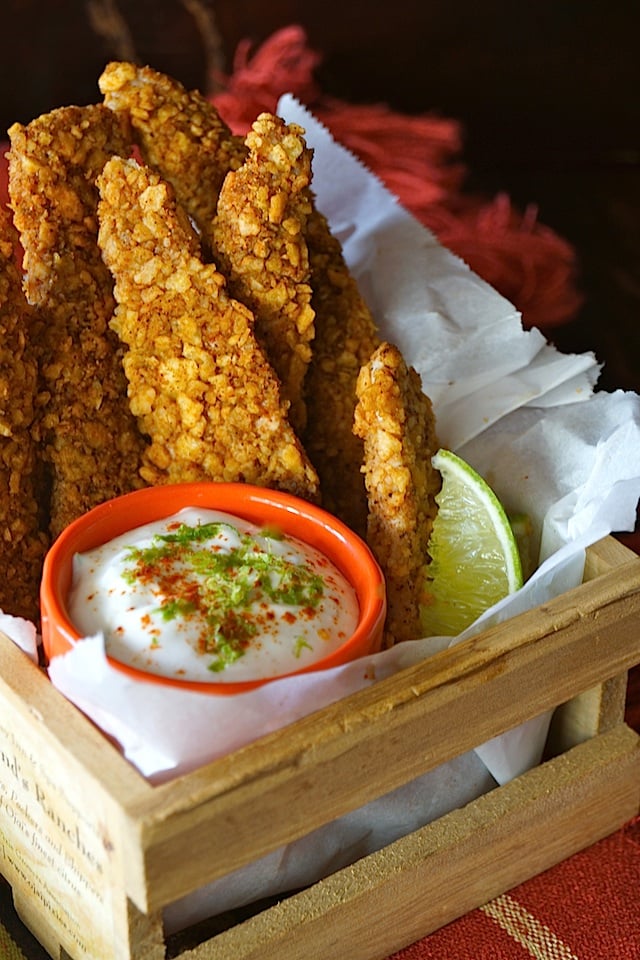 Tortilla Chip Crusted Chicken Strips in a wooden basket iwth parchment, orange bowl with sauce and lime