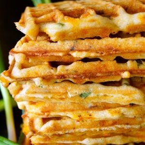 Stack of several Bacon Chedder Waffles with fresh scallions and black background.