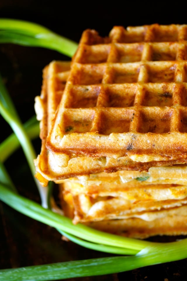 A small stack of Bacon Cheddar Gluten-Free Waffles with several whole, green scallions.