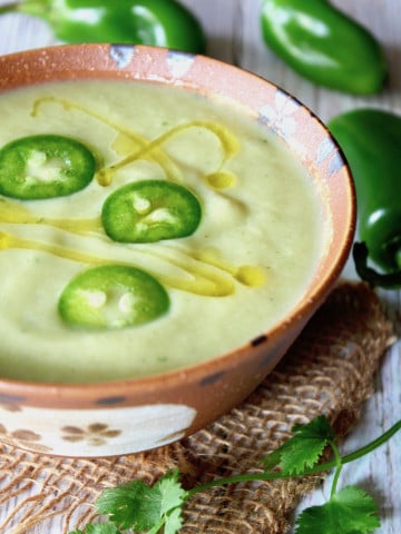 Cream of Jalapeno Cauliflower soup in rust-colored bowl with slices of jalapeno on top