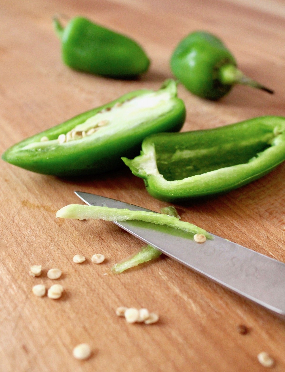 A few halved jalapenos on cutting board with paring knife.