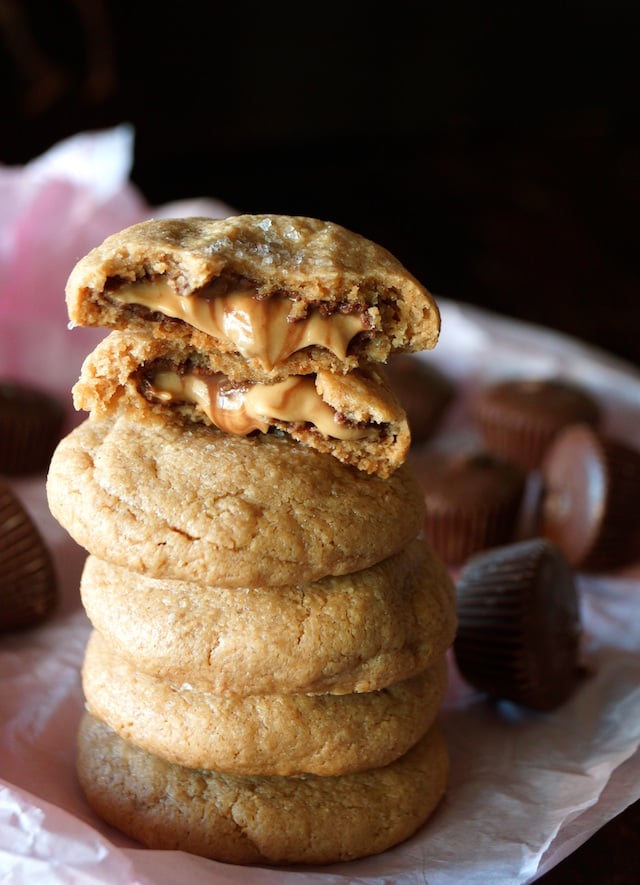 a stack of several Double Peanut Butter Chocolate Cookies, with the top one broken in half oozing with melting peanut butter