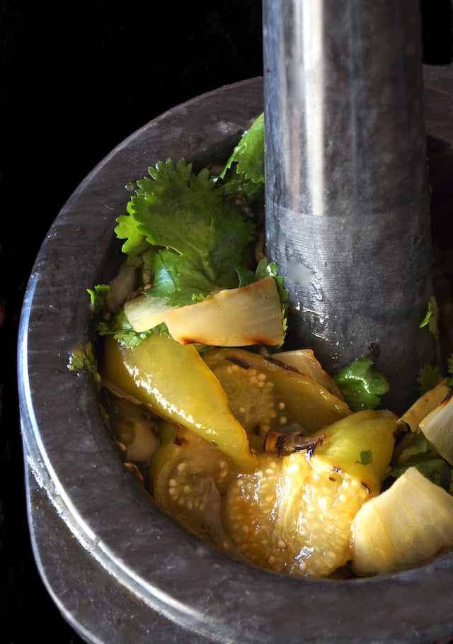 mortar with pestle with tomatillos, peppers, onion and cilantro