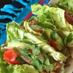 a few lettuce tacos with tomato and cilantro on narrow plate
