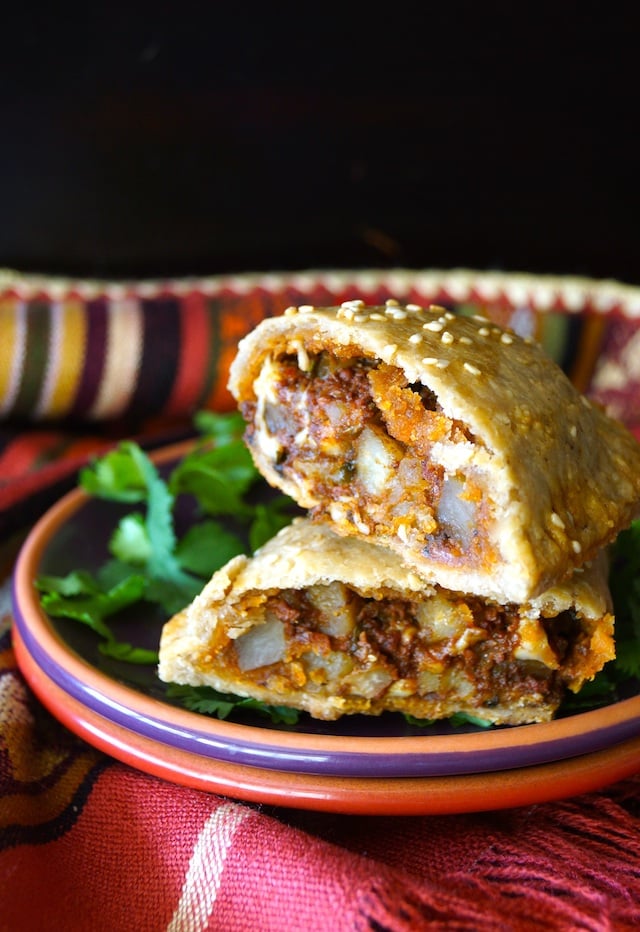 One Potato Chorizo Hand Pie, sliced in half on a purple plate with bright green cilantro.