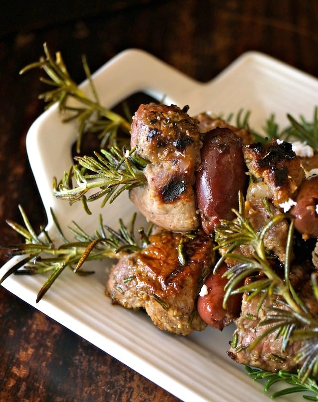 With fresh rosemary sprigs everywhere, a white platter with Rosemary Lamb Skewers