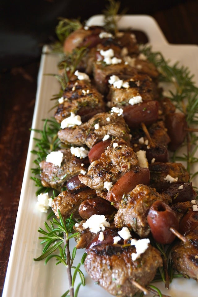 Rosemary Lamb Skewers sprinkled with fresh white Feta cheese crumbles on a narrow what platter.