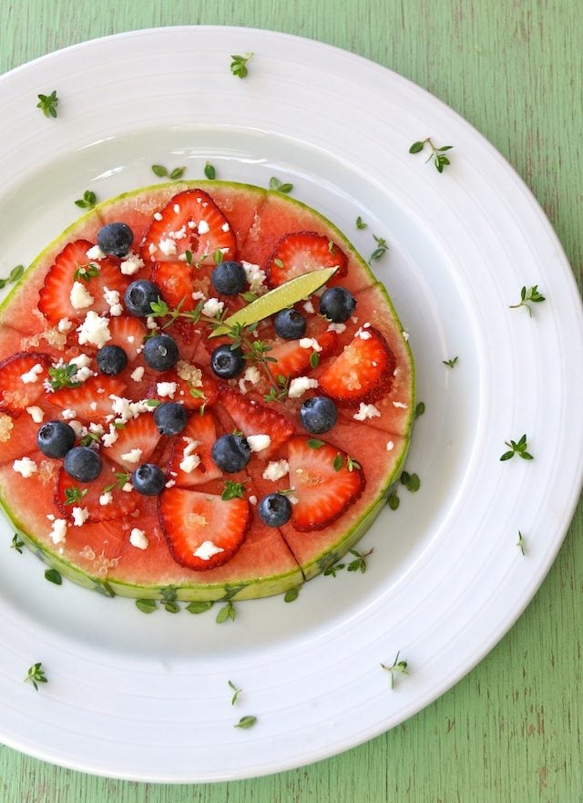 Whole Watermelon Pizza on a white plate with fresh thyme springs.