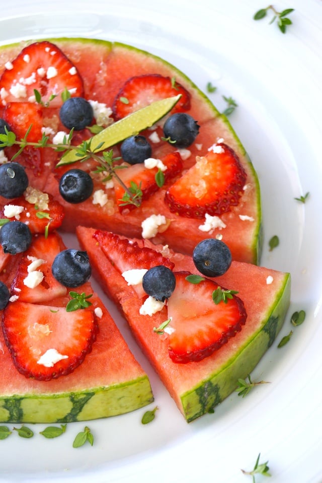 Sliced Watermelon Pizza Recipe with Lime, with one wedge slightly removed, with fresh blueberries, strawberries and thyme.