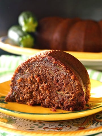 Large slice of chocolate zucchini bundt cake on a golden-colored, ceramic plate.