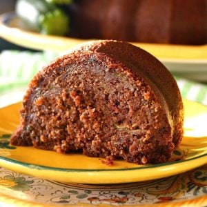 One large slice of chocolate zucchini bundt cake on a golden-colored, ceramic plate.