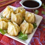 Several round dumplings on a white square plate with a small soy sauce dish in the background.