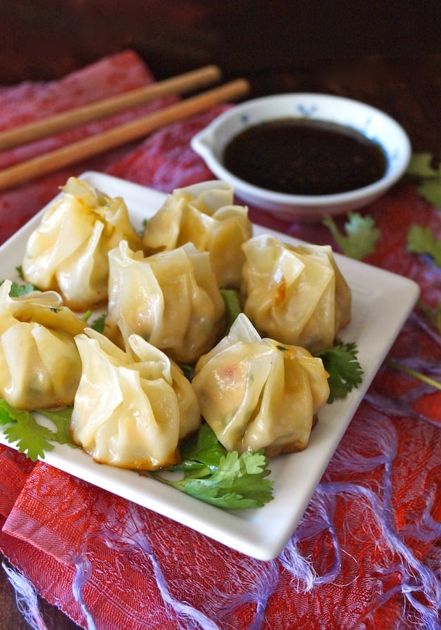 seven dumplings on a white dish with cilantro and a bowl of dark sauce