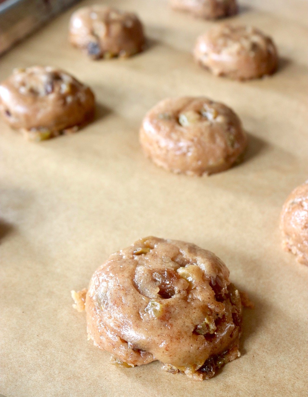 A few round balls of cookie dough with raisins that have been gently flattened, on parchment paper.