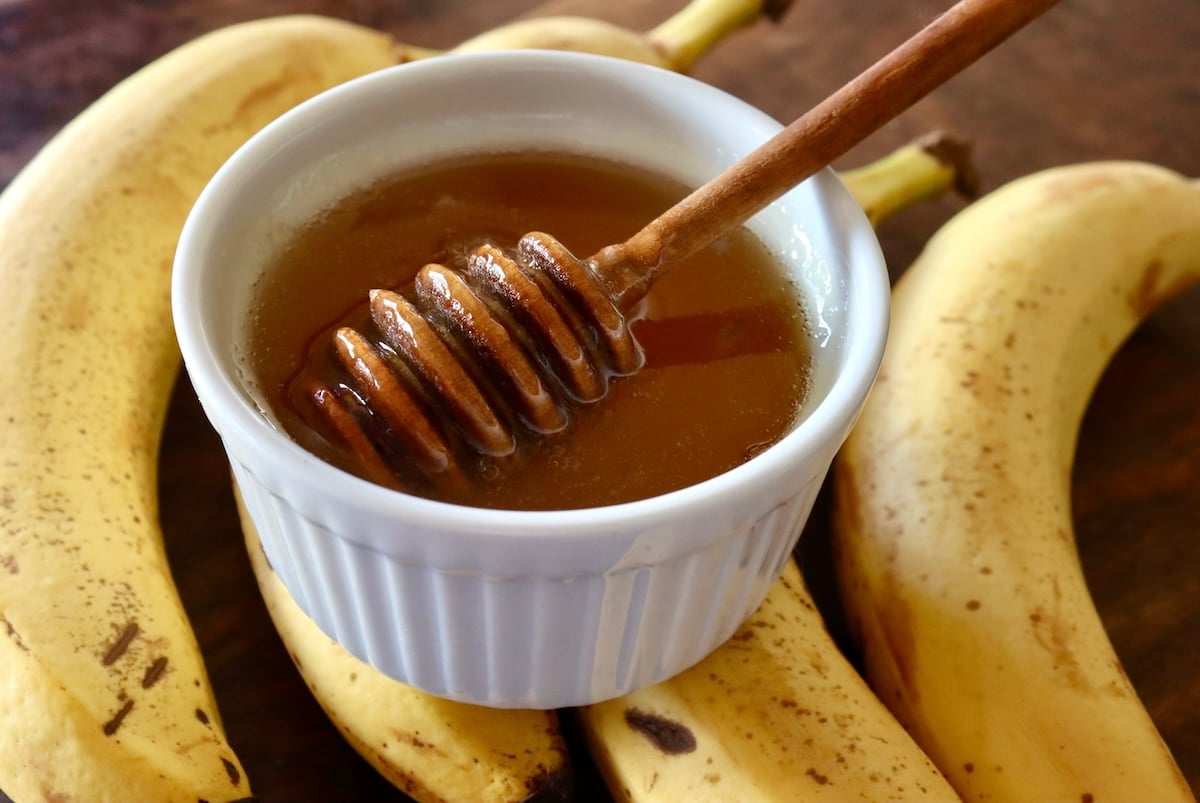 Honey in a white ramekin with a wooden honey spool, on top of 4 bananas.