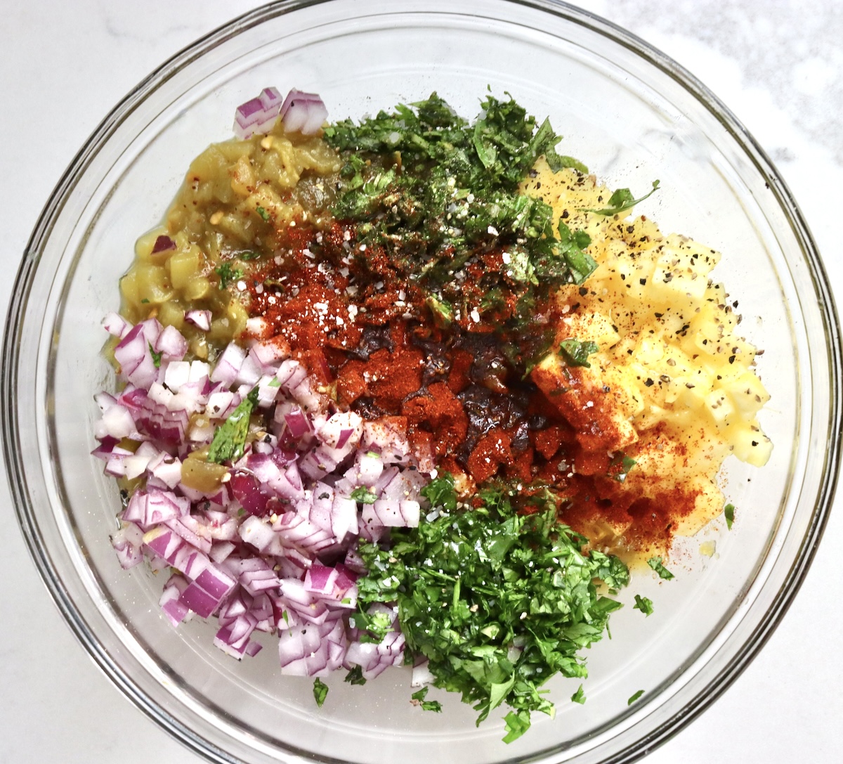Pineapple-Salsa-Recipe Chopped ingredients for pineapple salsa in a glass bowl - red onion, pineapple, grenn chile, cilantro, basil, and chili powder.