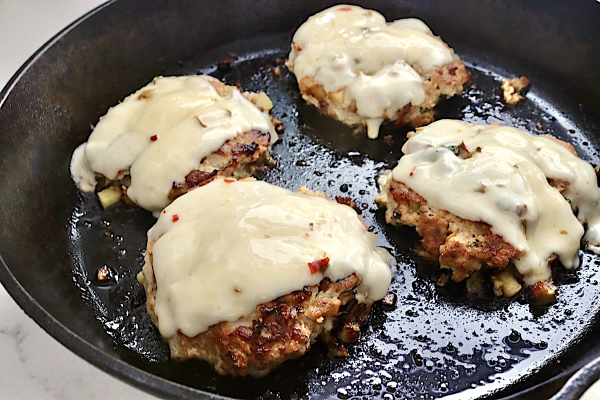 Hawaiian-Turkey-Burger-Recipe Cooked turkey pineapple burgers in a cast iron skillet, with melted cheese.